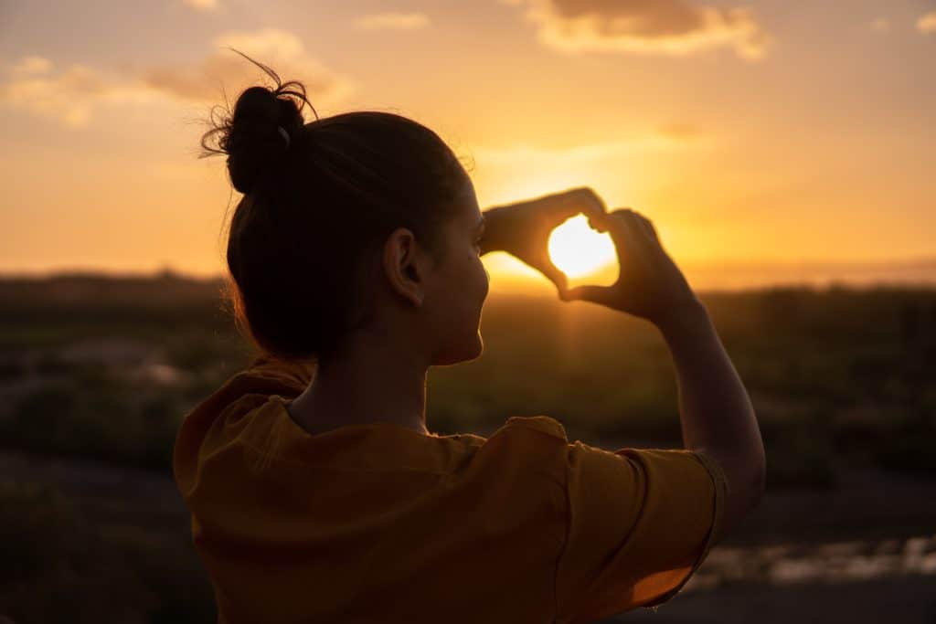 Lady making a heart in a sunset background